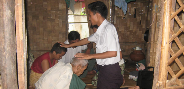 Native missionary lays hands on a sick buddhist as prayers are offerd to God for healing
